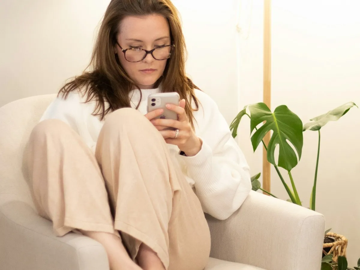 A person curled up in an armchair, reading on their phone.